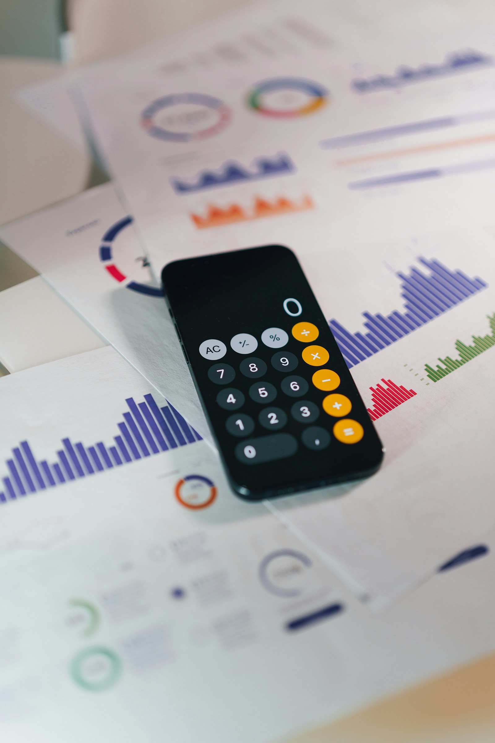 A calculator app on a phone resting on printed financial charts